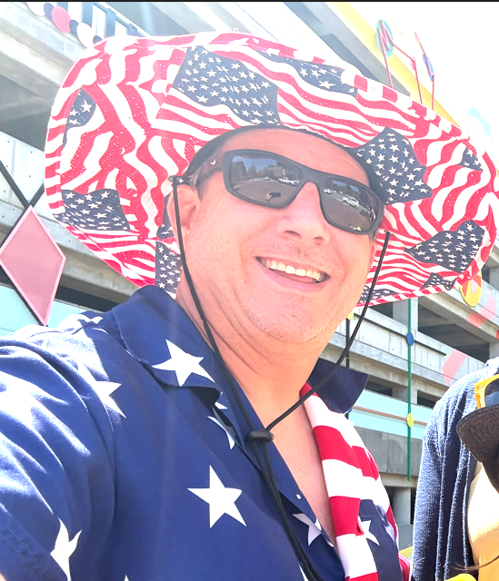 Mike smiling outdoors in a stars-and-stripes hat and shirt